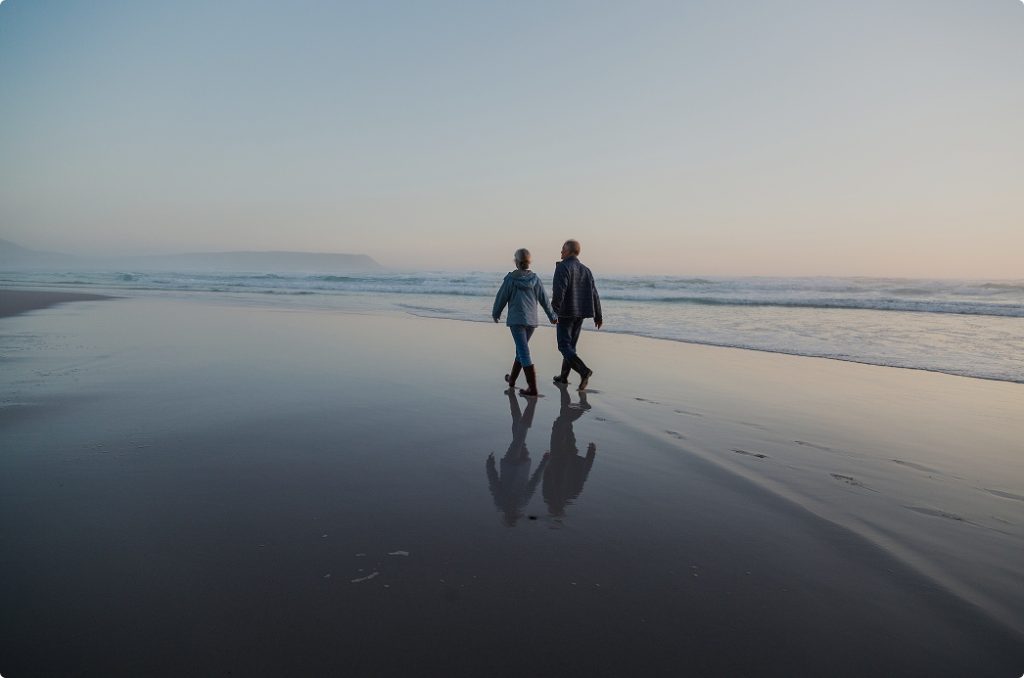 An older couple walking hand in hand on the beach.